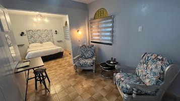 A room with a bed, two chairs, a small table, and a wall-mounted heater.