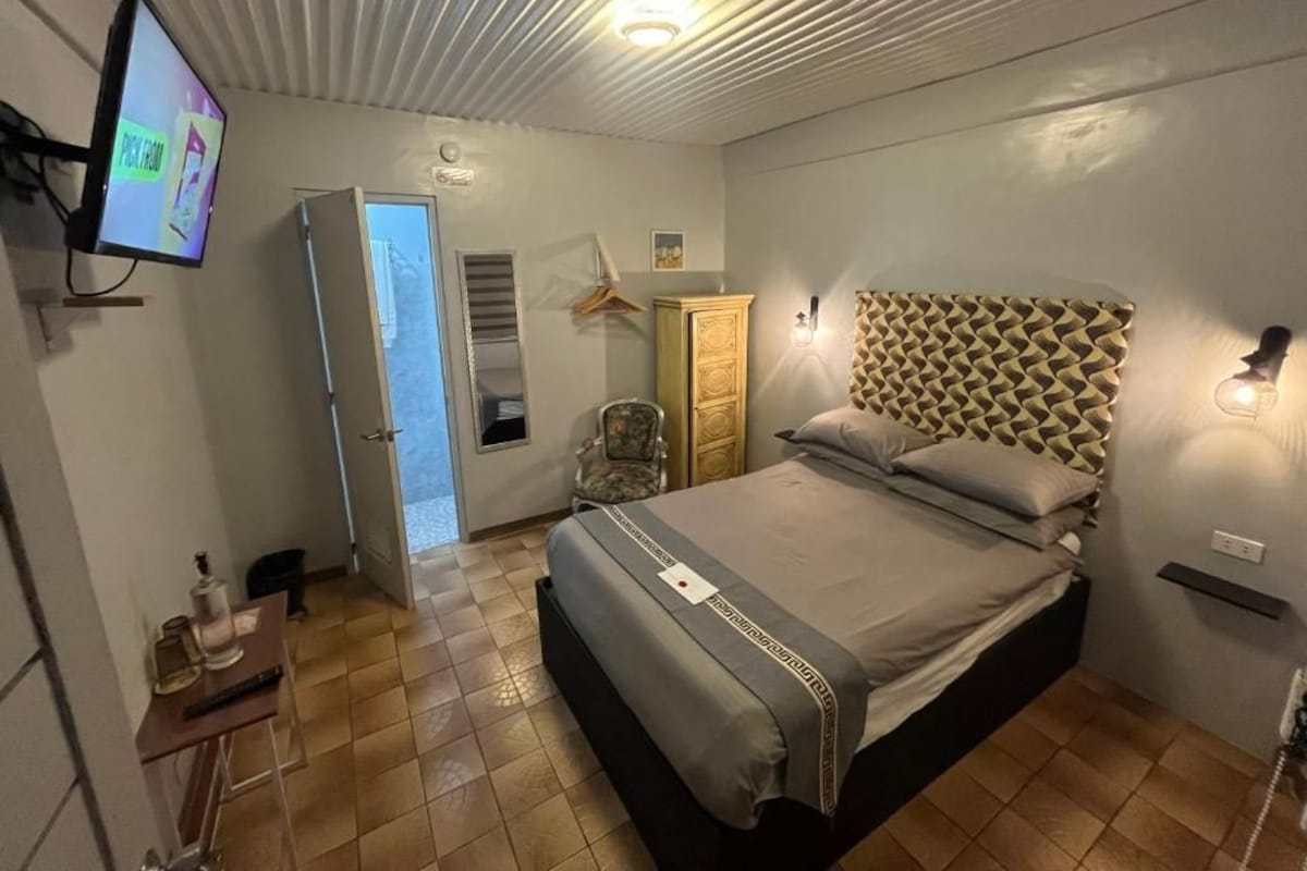 A bedroom with a bed, a television, a wardrobe, and a door leading to another room.