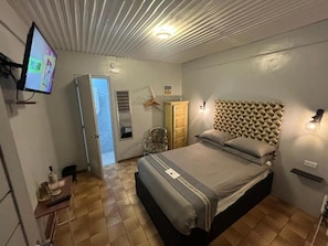 Un dormitorio con cama, televisión, armario y puerta que da a otra habitación.