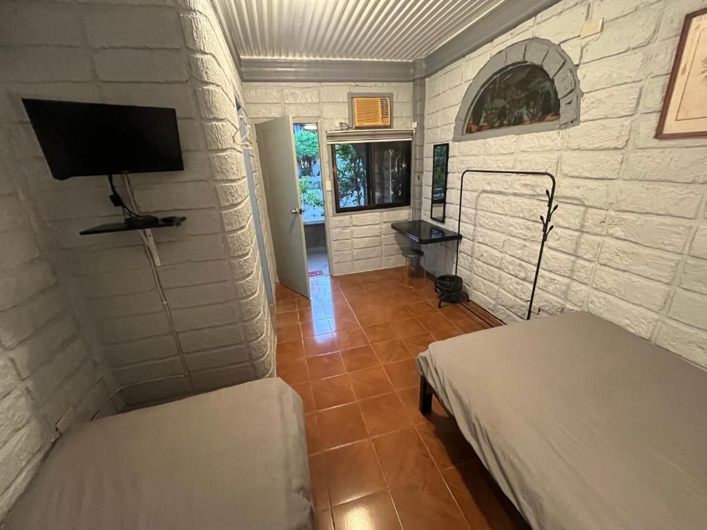 Una habitación con paredes de ladrillo blanco, un televisor de pantalla plana montado en la pared, una ventana con vistas a zonas verdes y una cama con cabecera.