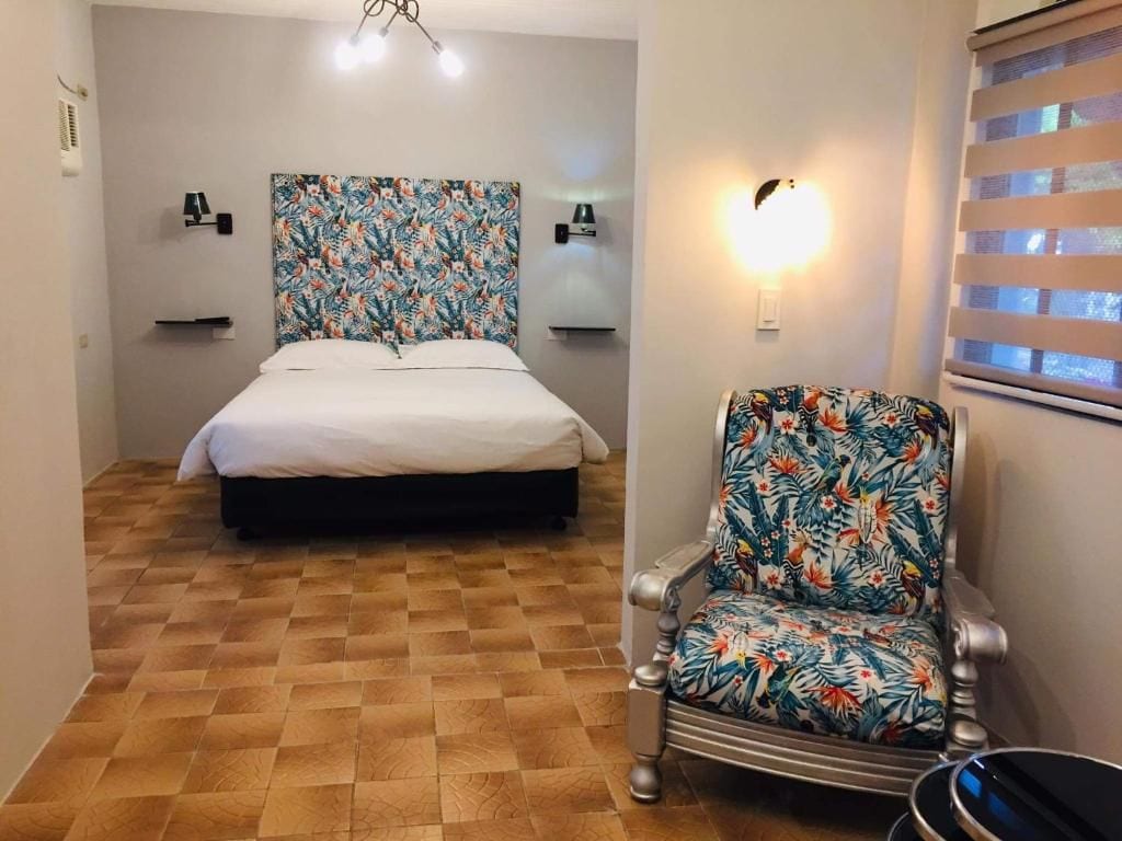 A bedroom with a bed, a chair, a wall-mounted light, and a window with blinds.