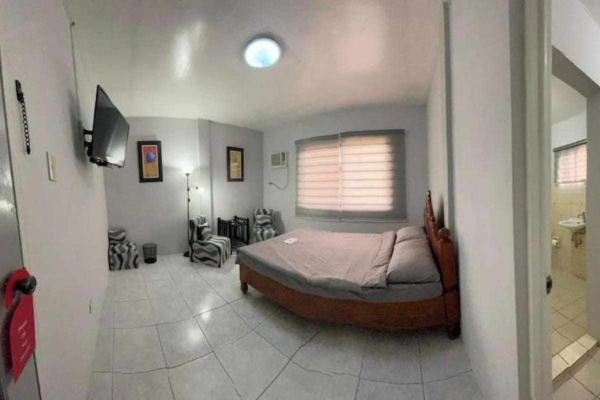 A bedroom with a bed, a chair, a desk, and a window.
