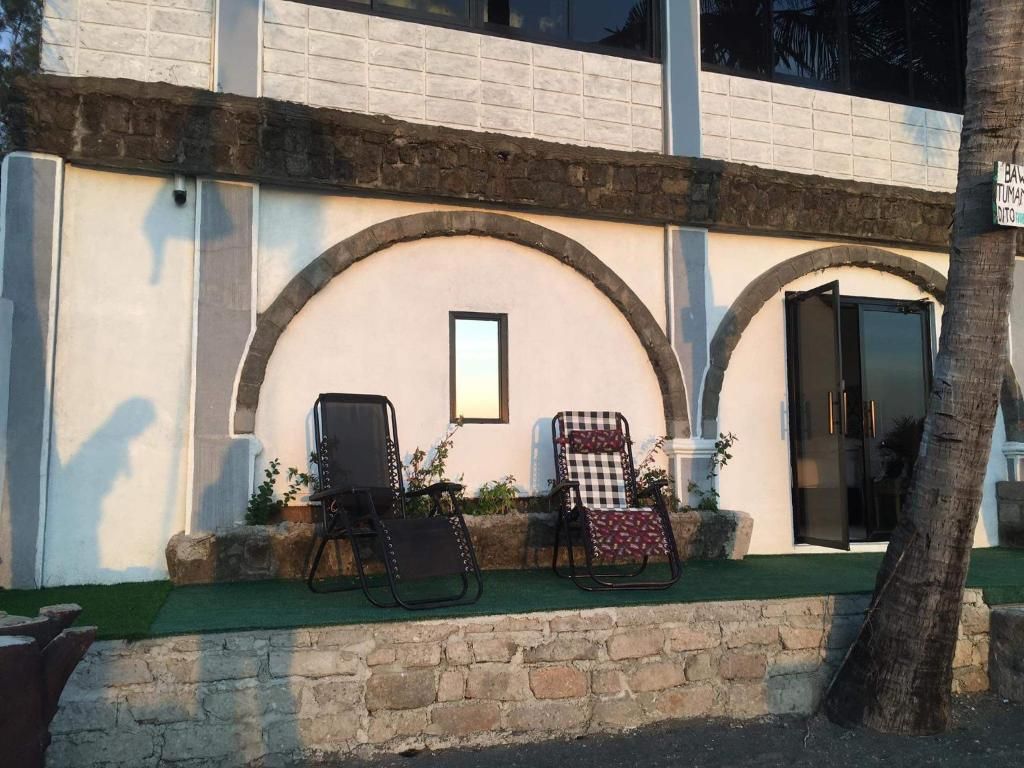 Un edificio con fachada de piedra, dos puertas arqueadas y una ventana pequeña. Hay dos sillas afuera, una con estampado de cuadros y otra de color liso.
