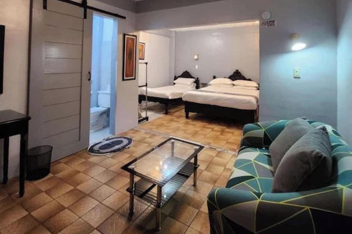 A compact hotel room with a bed, a sofa, a small table, and a ceiling with a light fixture.