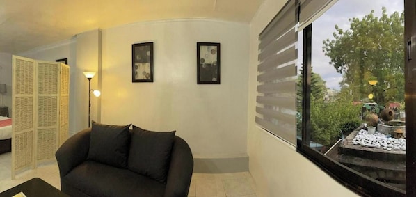 A room with a black sofa, a window with a view of greenery, and two framed pictures on the wall.