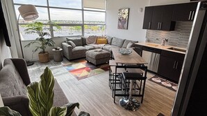 A modern living room with a sofa, a dining table, and a kitchen area with cabinets and a refrigerator.