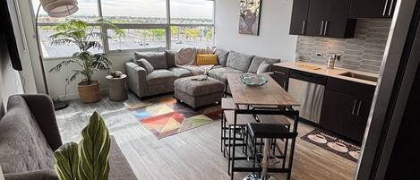 Uma sala de estar moderna com sofá, mesa de jantar e cozinha equipada com armários e geladeira.