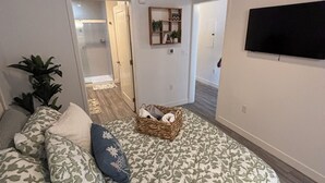 A bedroom with a bed, a TV, a door leading to another room, and a plant.