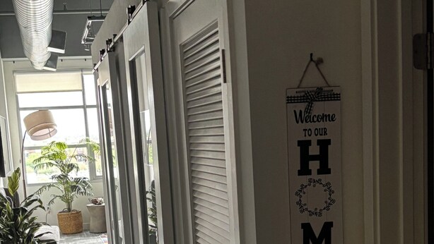 A hallway with a sign reading 'Welcome to our HOME' on the wall, potted plants, and a modern ceiling design.