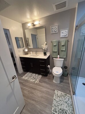 A bathroom with a toilet, sink, mirror, and a shower area.