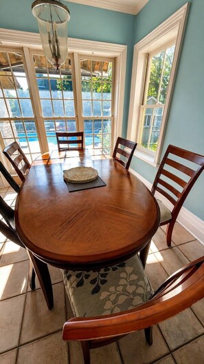 Een eetgedeelte met een ronde houten tafel, zes stoelen en een kroonluchter.