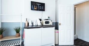A kitchenette with a microwave, toaster, and coffee maker on a countertop, a small potted plant, and a TV mounted on the wall displaying a language selection menu. - The Bay Apart-Hotel by Guestz (Morecambe)