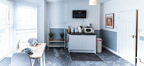 A compact kitchen with a microwave, toaster, and sink, a small dining table with chairs, a TV mounted on the wall, and a door leading to another room. - The Bay Apart-Hotel by Guestz (Morecambe)