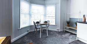 Habitació d'angle amb taula de dinar, dues cadires, una petita prestatgeria amb plantes i un radiador blanc.