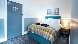 Ein Hotelzimmer mit Bett, Nachttisch, Lampe, Tür und einem Wandbild.