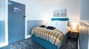 A hotel room with a bed, a nightstand, a lamp, a door, and a wall-mounted painting. - The Bay Apart-Hotel by Guestz (Morecambe)