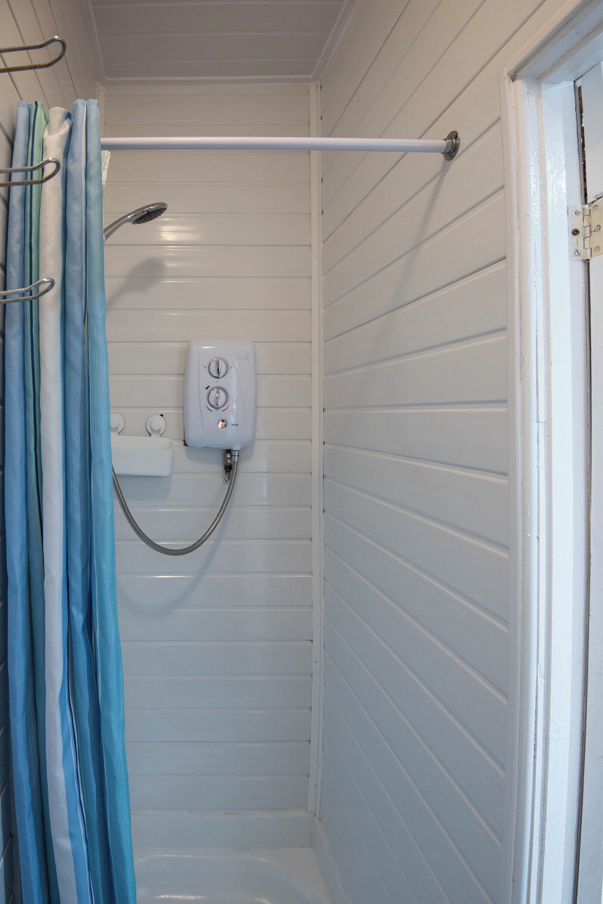 Zona de ducha con cabezal de ducha de mano, panel de control y barra para cortina.