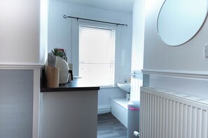 A bathroom with a toilet, sink, and window with blinds. - The Bay Apart-Hotel by Guestz (Morecambe)