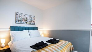 Ein Hotelzimmer mit Bett, kariertem Bettbezug, Kopfteil, Nachttisch mit Lampe und einem Wandbild.