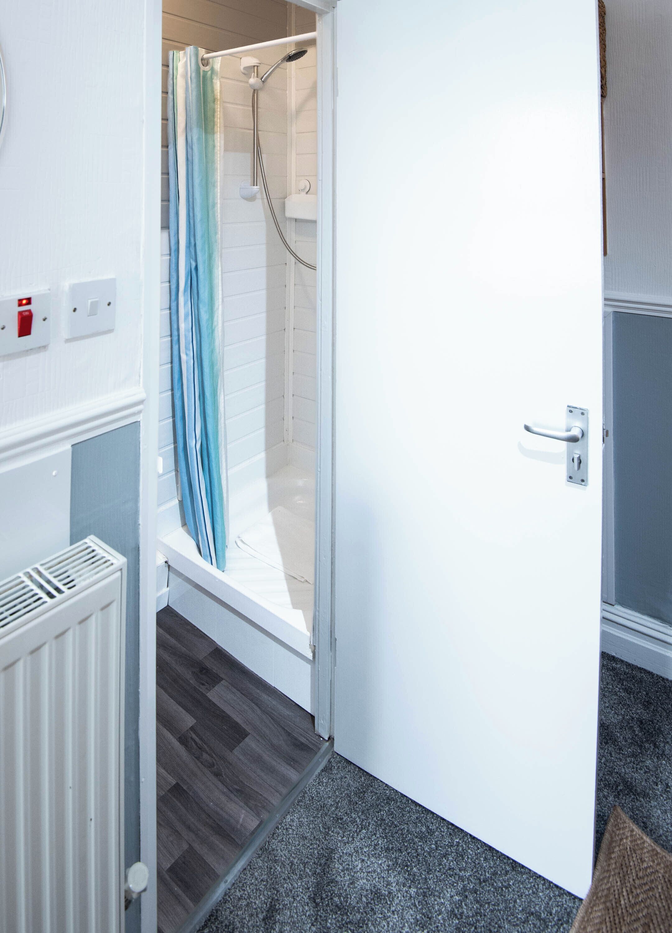 Un bagno con doccia, una porta bianca, un termosifone e un tappeto grigio.