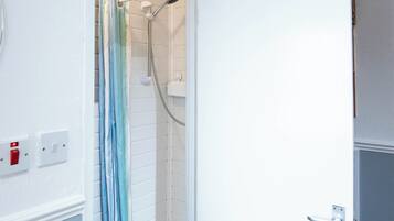 Un bagno con doccia, una porta bianca, un termosifone e un tappeto grigio.