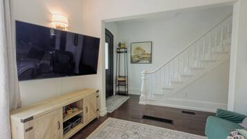 A living room with a flat-screen TV, wooden entertainment unit, and a staircase with white balusters.