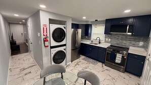 Eine moderne Küche mit dunklen Schränken, Edelstahlgeräten, einem Glastisch und einem an der Wand befestigten Feuerlöscher.