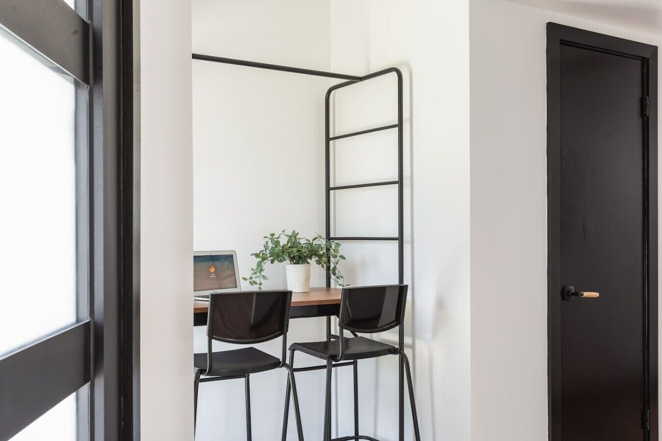 A room with a desk, two chairs, a potted plant, and a door.