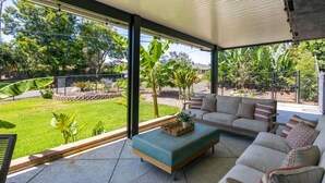 Un espacio de estar al aire libre cubierto con vistas a un jardín ajardinado.