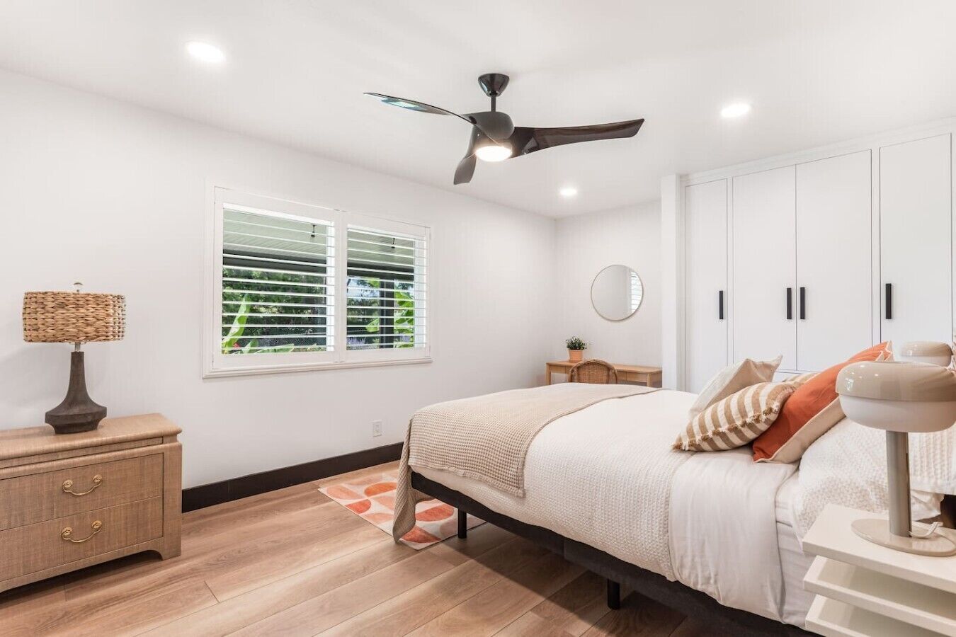A bedroom with a bed, bedside table, lamp, window, ceiling fan, and wardrobe.