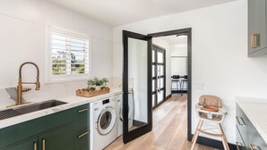 Una cocina moderna con lavadora integrada, un lavamanos con grifo dorado y una ventana con persianas.