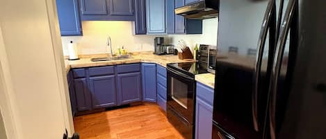 Una cocina con suelo de madera, armarios azules y un refrigerador negro.