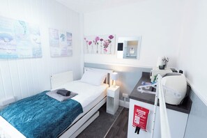 A hotel room with a bed, a nightstand, a desk with a computer, a mirror, and a red fire blanket. - The Bay Apart-Hotel by Guestz (Morecambe)
