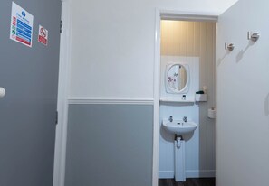 A bathroom with a white sink, a mirror, and a toilet. There are signs on the wall, including a fire action notice. - The Bay Apart-Hotel by Guestz (Morecambe)