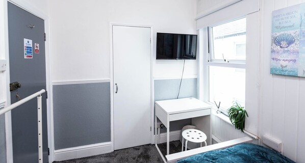 Une chambre à coucher avec un lit, un bureau, une chaise, une télévision, une porte et une fenêtre.