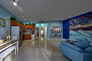 A modern living room with a blue sofa, a dining table with candles, and a kitchen in the background. - Tranquility 2Bed/2Bath/2K -5 Star DT Area -Hot Tub (Fort Lauderdale)