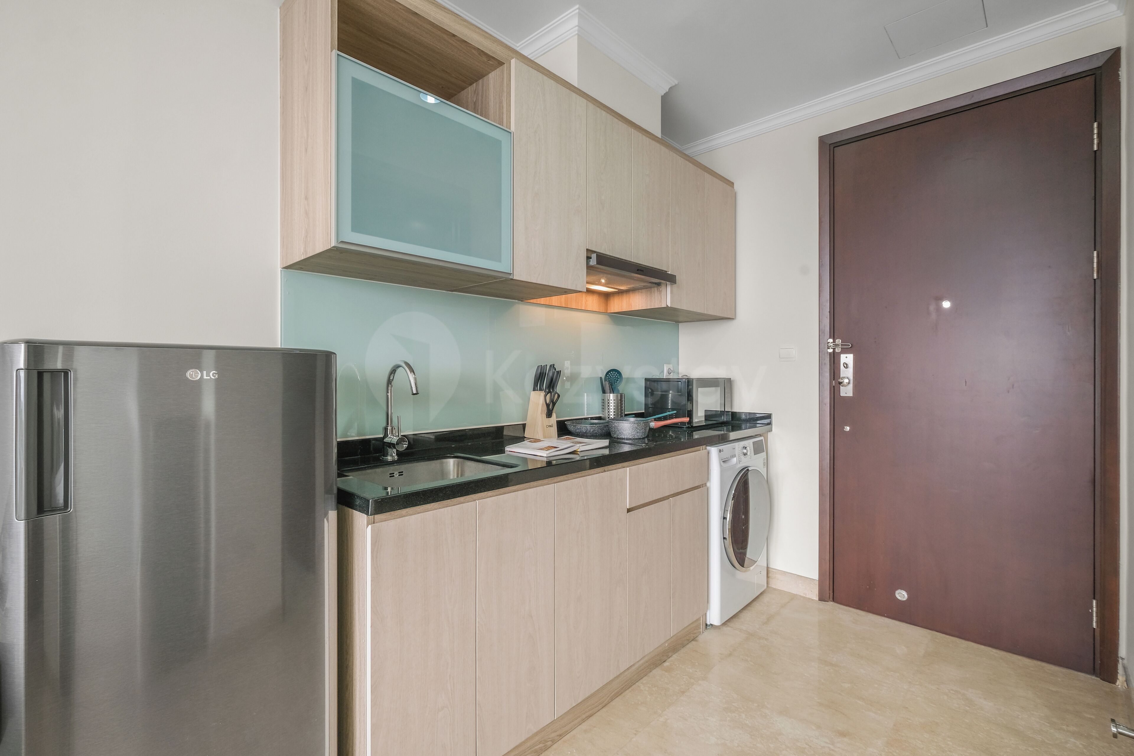 A compact kitchen with a stainless steel refrigerator, a microwave, a sink, and a washing machine.