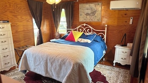 A bedroom with a bed, a nightstand, a dresser, a ceiling fan, a window with curtains, and a wall-mounted air conditioner. - Uncle Gary’s Wonky Cabin in Steinhatchee, FL (Steinhatchee)