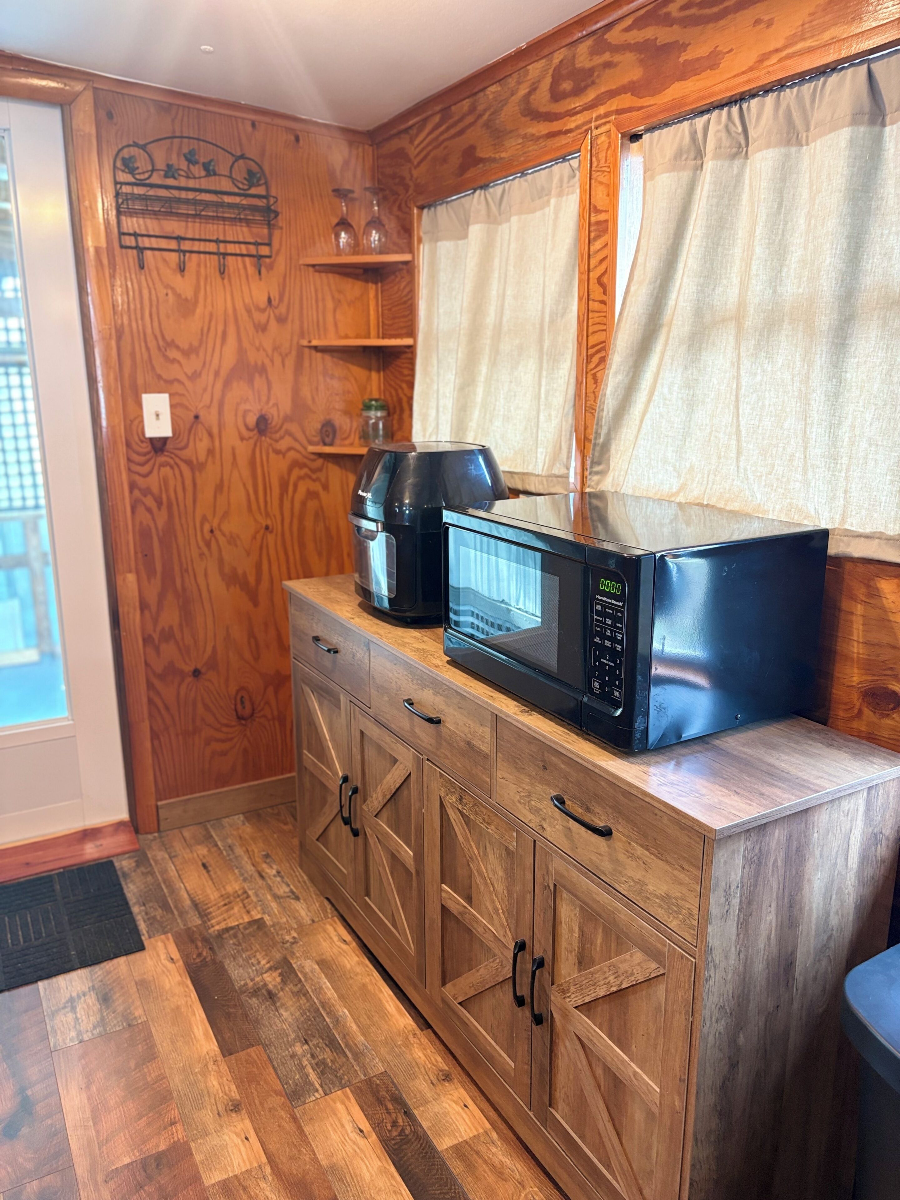 Une cuisine dotée de meubles en bois, d’une machine à café, d’un four à micro-ondes et d’une fenêtre avec des rideaux.