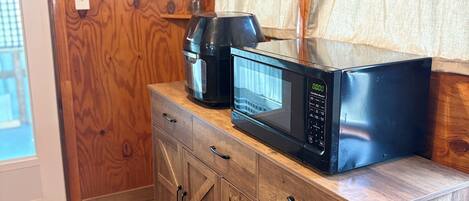 Een keuken met houten kastjes, een koffiezetapparaat, een magnetron en een raam met gordijnen.