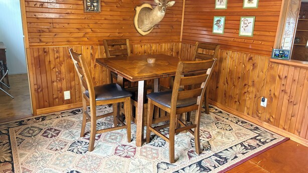 A wooden-paneled room with a round table and chairs, a mounted deer head, and framed pictures on the walls. - Uncle Gary’s Wonky Cabin in Steinhatchee, FL (Steinhatchee)