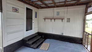 A room with a wooden ceiling, a white door, and a small set of steps leading to a door. There are signs on the wall and a shelf above the steps. - Uncle Gary’s Wonky Cabin in Steinhatchee, FL (Steinhatchee)