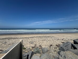 A beach with a wooden fence, large rocks, and a pier in the distance.