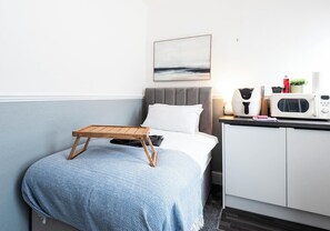 Quarto bem arrumado com cama, mesa de cabeceira e uma pequena área de cozinha.