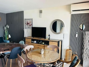 Ein modernes Wohnzimmer mit Fernseher, Esstisch, Stühlen und einer Couch.