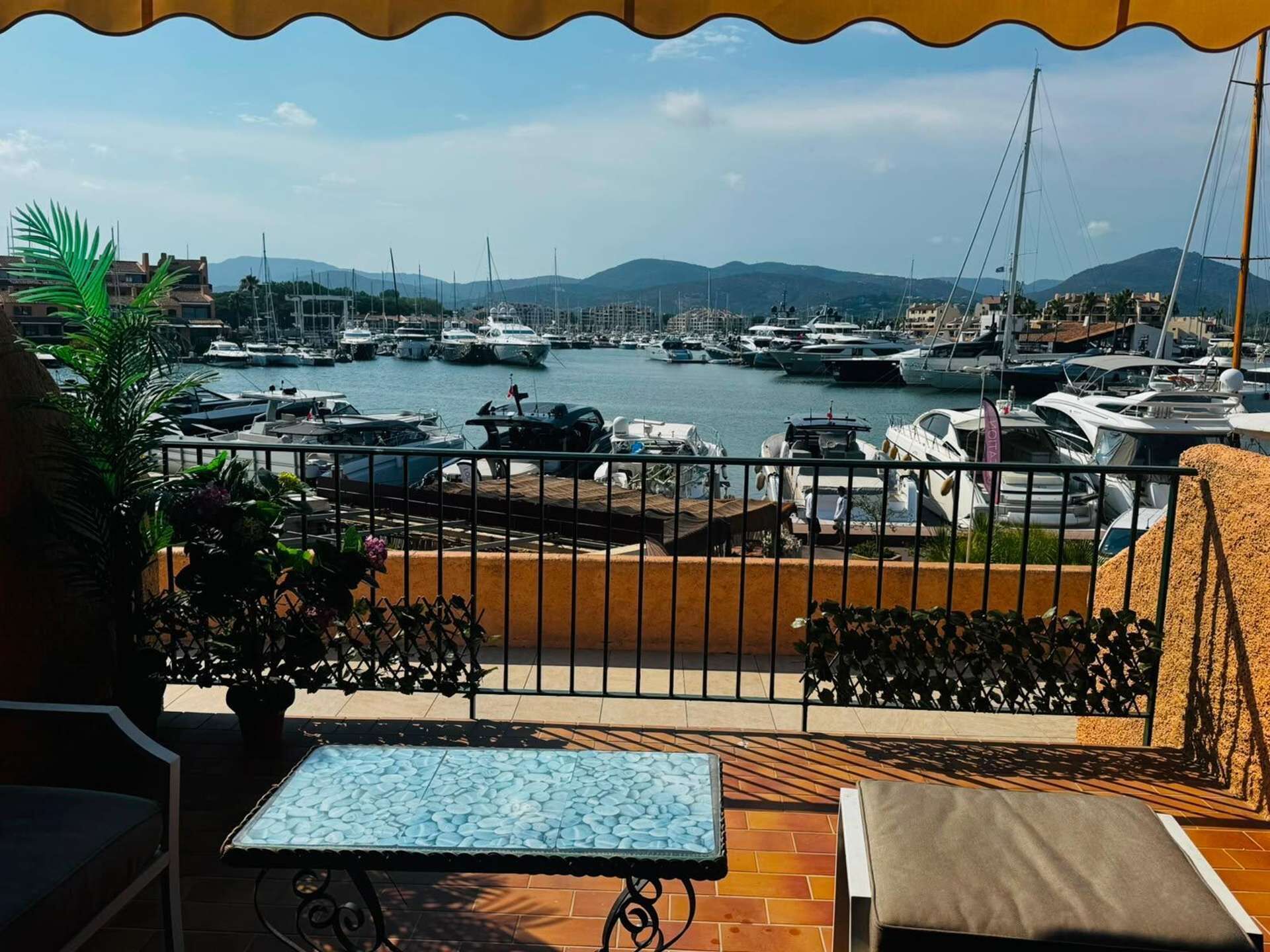 A balcony with a view of a marina, a table, and chairs.