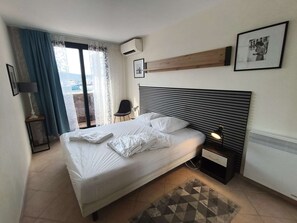 Ein Hotelzimmer mit Bett, Nachttisch, Lampe, Bilderrahmen und einem Fenster mit Vorhängen.