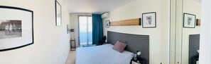 Ein Hotelzimmer mit einem Bett, einem Nachttisch, Vorhängen vor dem Fenster und gerahmten Bildern an den Wänden.