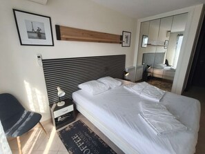 A modern bedroom with a large bed, bedside tables, a chair, a mirror, and framed pictures on the wall. - Appt T2  climatisé  avec Vue sur le Port À deux pas de la plage et aux portes de Saint-Tropez (COGOLIN)