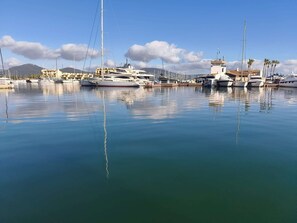 Eine Marina mit mehreren Yachten an den Liegen, ruhigem Wasser und Gebäuden im Hintergrund.